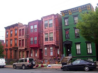 A group of five three-story brick rowhouses, two and three bays wide, on an urban street. The one on the right is painted green, the three in the middle have projecting bays on the upper stories and the leftmost one is unpainted.