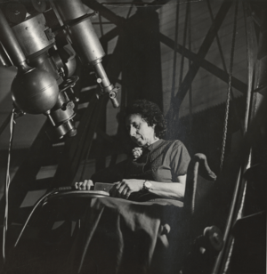 White woman seated at a telescope.