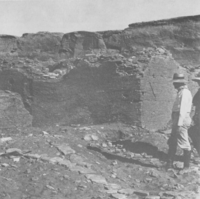 A black-and-white photo of a man standing next to a large ruin