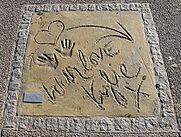 Handprints in a sand, with a heart-shaped and arrow drawings and written words "With love Kylie x".