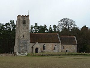 A stone church with red tiled roofs seen from the south, showing a battlemented tower, a nave with a south porch, and a chancel at a lower level