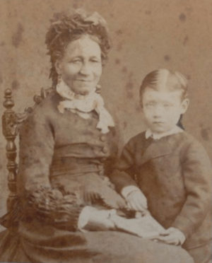 Photograph of a dark-skinned woman in a Victorian-era dress seated next to a standing  child