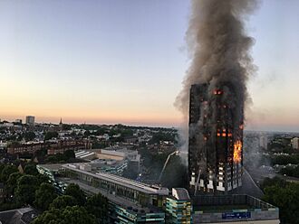 A tower block (Grenfell Tower) burning on nearly all floors with large amounts of smoke rising, and water being sprayed at the building from firefighters.