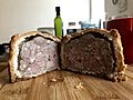 Large pork pie cut in half on a cutting bord made of wood