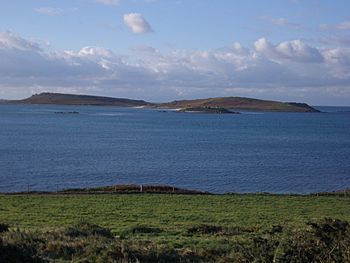 Looking from the grassy shore of Tresco, across the calm water, to the low twin hills of Samson
