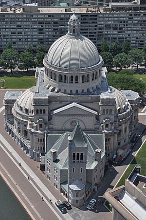 Aerial photograph of a triangular lot between roads and their sidewalks. The lot contains a small, Romanesque church filling the front point to the sidewalks, connected to a much larger and impressive domed, Neoclassical building behind it, filling the lot to the sidewalks to the left and right.