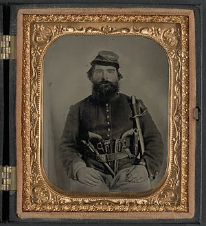 A. J. Blue, cavalry soldier in Union shell jacket and bummer cap with three Remington revolvers in his belt, holding a sword LCCN2011645425