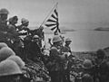 alt=Historic photograph of Japanese troops raising the Imperial battle flag on Kiska Island.