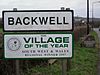 Road signs with Backwell in black writing on white background and below it another sign saying village of the year South West and Wales regional winner 1997.