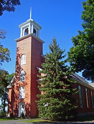 A brick building with a pine tree in front and a tower with white cupola
