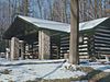 A snow-covered log cabin with a porch supported by stone pillars