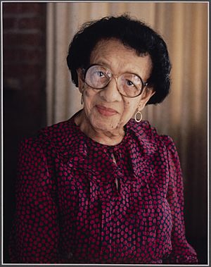 Photo portrait African American woman wearing pink ruffled blouse and glasses with short cropped black hair.