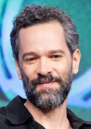 46-year-old man with dark hair and a beard smiling towards the camera
