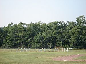 Green field with green trees in the background. Large, wooden letters in the foreground spell "C A M P  W E S T M O N T."
