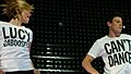 Agron and Cory Monteith, as their characters from "Glee", dance enthusiastically wearing simple white t-shirts with black text: Agron's reads "Lucy Caboosey" and Monteith's "Can't Dance".