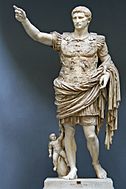 A marble statue of the Emperor Augustus. He stands with one arm raised as if in command. Augustus is portrayed as a man of about thirty five, with short hair and clean shaven. He wears Roman military uniform of a breast plate, leather accoutrements and a cloak over a short tunic. The breastplate is decorated with symbolic figures. As a work of art, the statue displays high technical mastery.