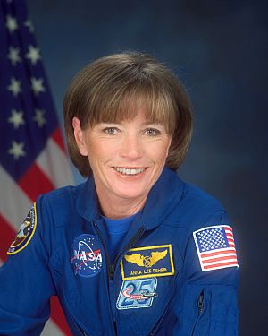 Formal portrait of astronaut in a flight suit displaying mission patches with an American flag in the background