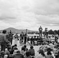 Man standing on stage addressing a crowd with a view of a mountain in the background