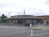 A low circular building with a wide awning is surmounted by a glazed column with a metal ball on the top