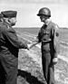 Two white men in military dress uniform shaking hands. One is an Older man and on is a young man.