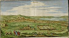 Two men and a lion in the foreground of a landscape showing a green valley across which can be seen a densely-built city