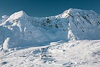 "A view from above of approximately twenty snow-covered buildings, backed immediately by large, snow-covered mountains in shadow."