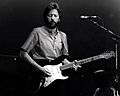 A black and white photograph of Eric Clapton with a guitar on stage