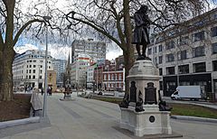 Northern end of The Centre, Bristol, before the removal of statue of slave trader Edward Colston. A paved area with mature trees surrounded by 19th and 20th century buildings.