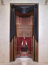The courtroom doors of the Supreme Court draped in black. Through the open doors is visible Ginsburg's seat and the bench before the seat, each also draped in black.
