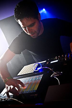 Gui Boratto leaning over a set of DJ modules onstage, mid-performance