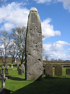 a cemetery over which towers a large standing stone with some sort of cap