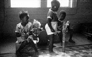 Three black children playing with dolls and alphabet blocks at Delta Cooperative