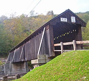 A wooden covered bridge on stone and concrete abutments viewed from below and to the left