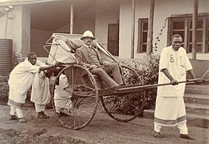 George Wilson seated in a rickshaw with four Ugandans in front and behind the vehicle - circa 1906-11
