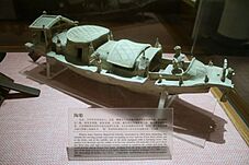 A pottery model of a boat with a steering rudder at the stern and a small sailor figurine standing on board