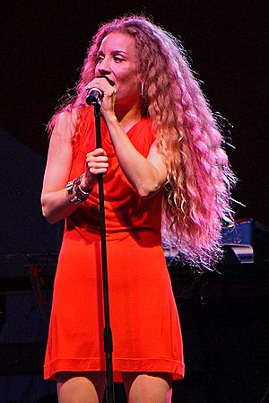 Amanda Marshall wearing a red, sleeveless dress, singing into a microphone onstage