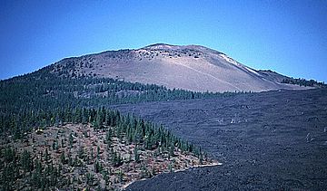 A gently sloping shield volcano with little forestation rises above lava flows.
