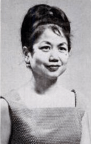 A smiling Filipina woman with dark hair in a bouffant updo, wearing sleeveless dress or top with a square neckline