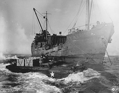A merchant ship unloads supplies into a DUKW (greyscale)